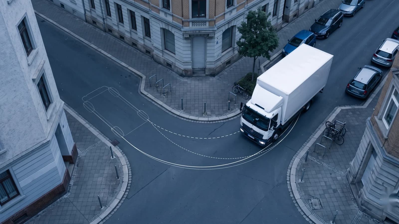 Luftaufnahme: weißer Koffer-Lkw biegt an einer engen europäischen Straßenecke ab, mit Overlay-Kurven, die den sofortigen Lenkbogen mit der weichen, lenkratenbegrenzten Spur vergleichen